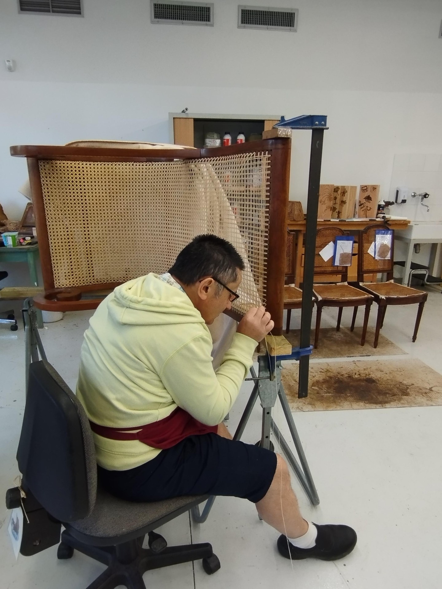 Artisan de l'atelier chaiserie en plein travail de cannage sur un dossier